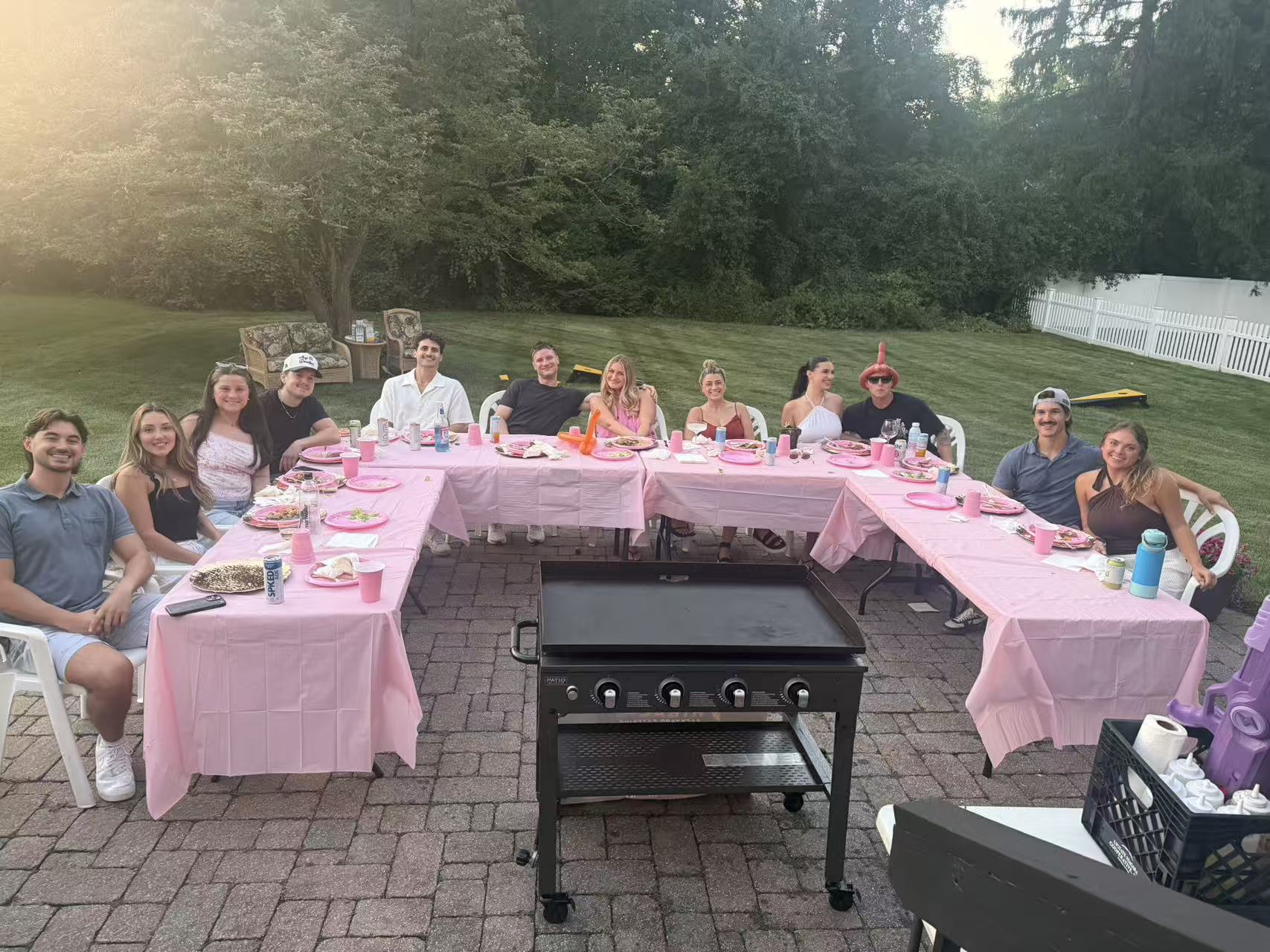 Large backyard hibachi party with pink tablecloths and a Go For Hibachi chef